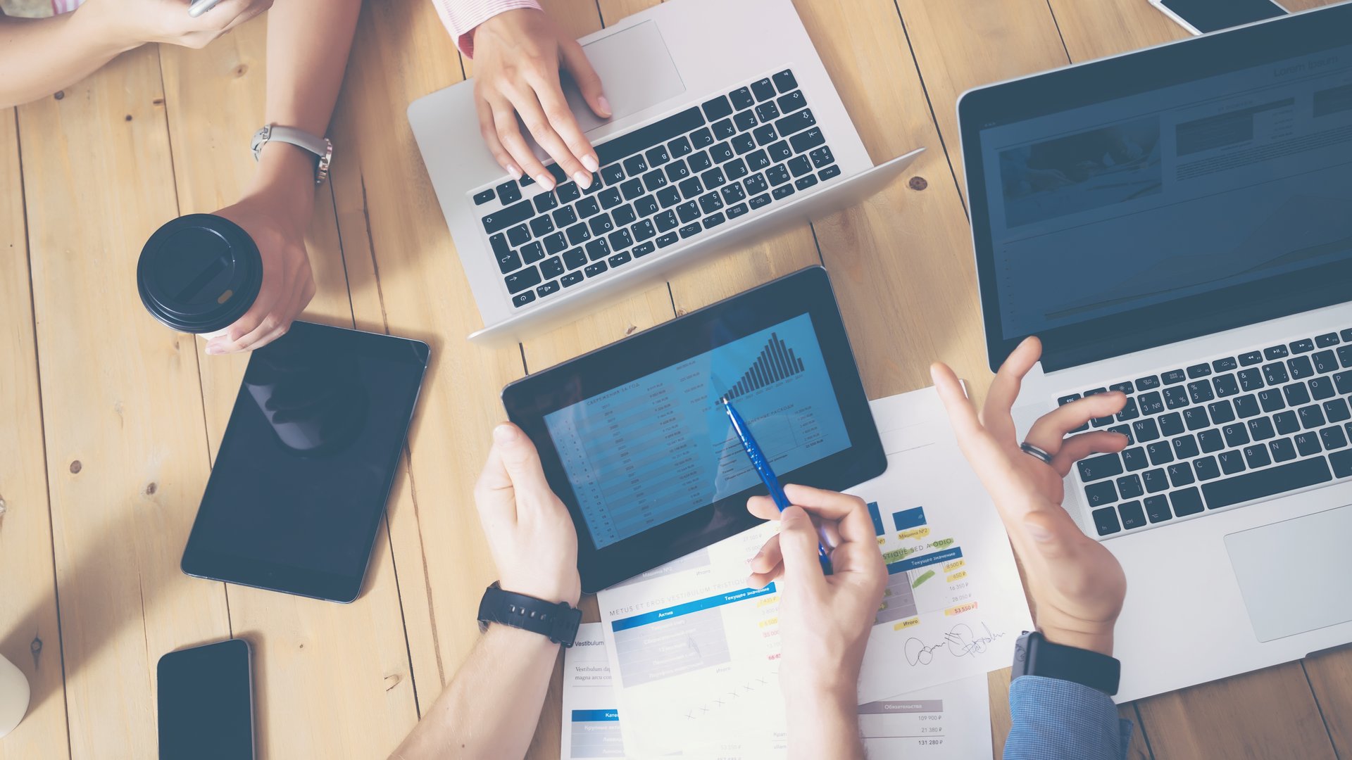 Generisches Büro, mehrere Hände die über einen Tisch greifen Laptops und Tablets auf dem tisch