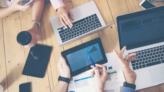 Generisches Büro, mehrere Hände die über einen Tisch greifen Laptops und Tablets auf dem tisch